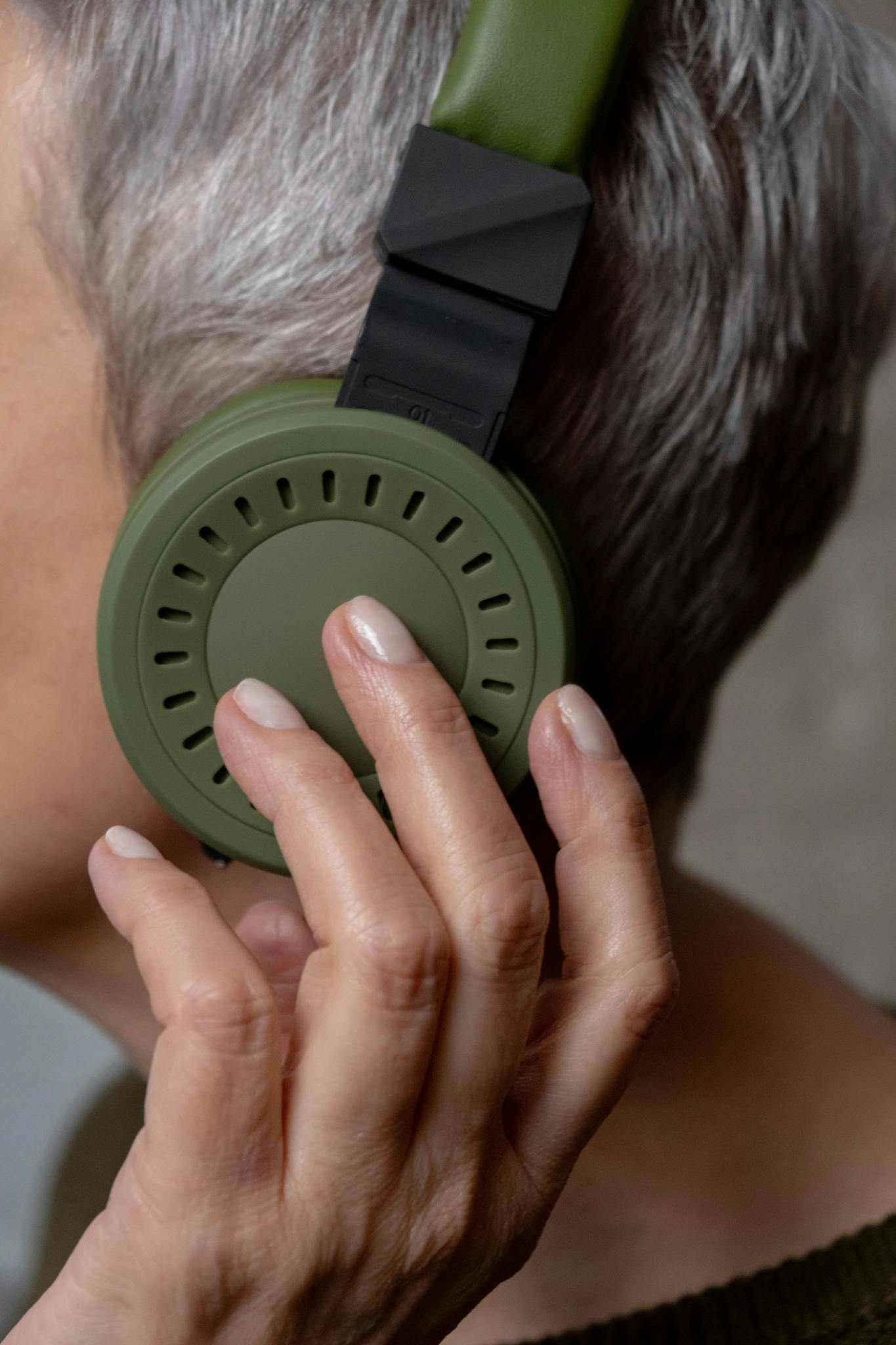 Close-up of a senior woman wearing green wireless headphones, listening to music.