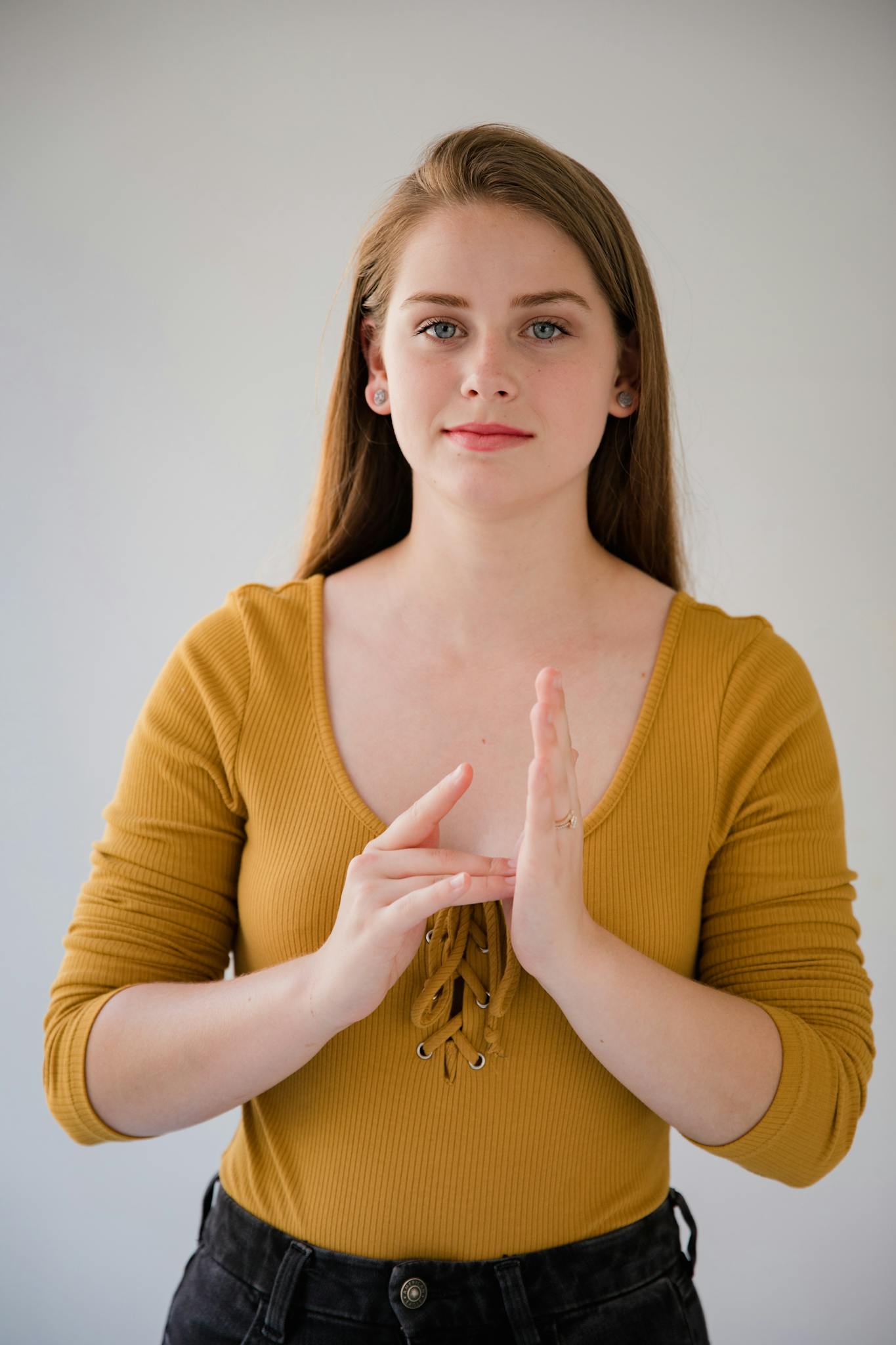 Portrait of a young woman gesturing in sign language, wearing a yellow top and looking at the camera.